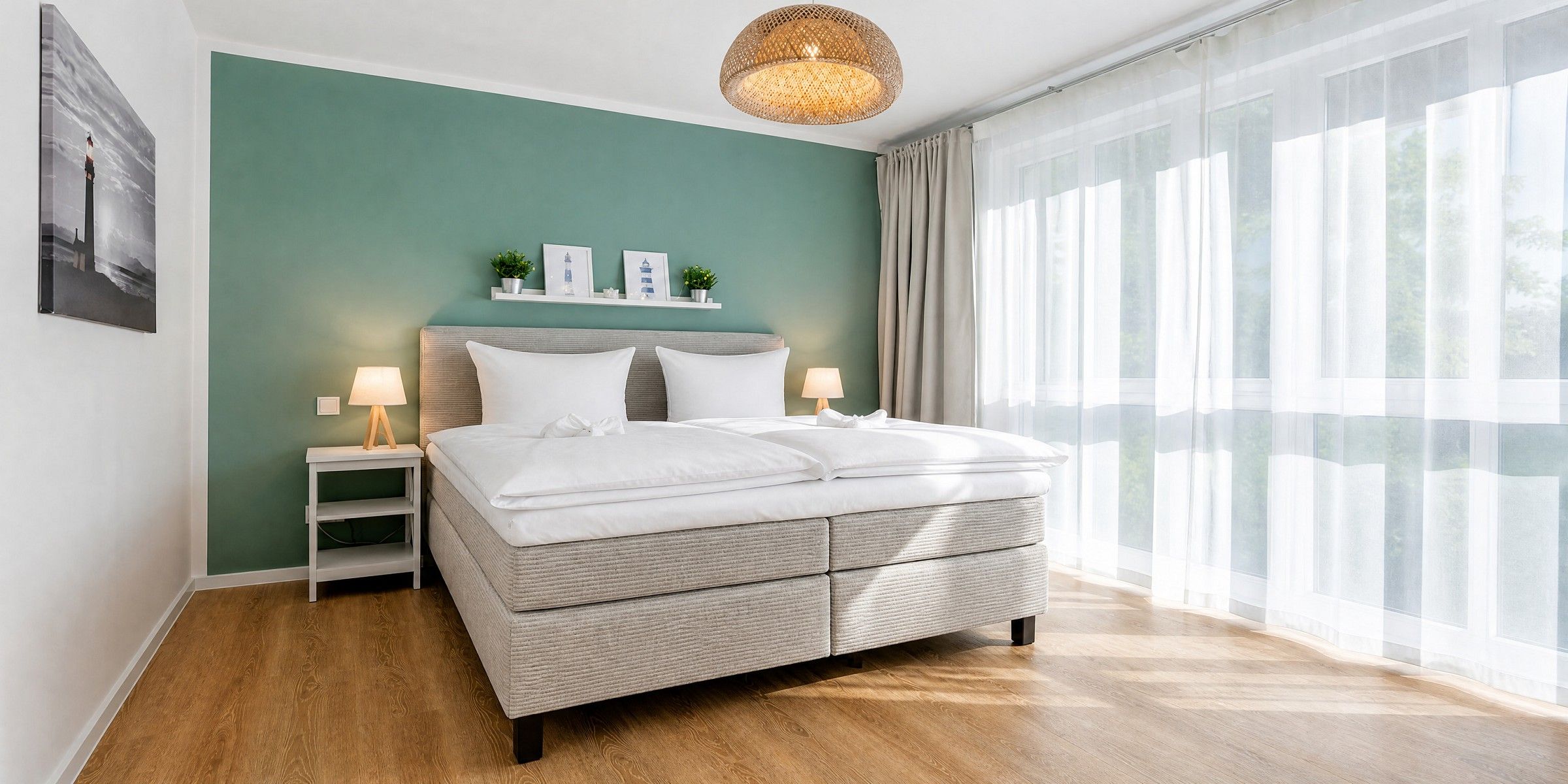 A modern bedroom with a large bed, bedside lamps, a wall-mounted shelf with decorative items, and a large window with sheer curtains.