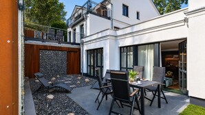 A modern house with a patio, outdoor seating, and a stone wall. - Beach shell vacation apartment at Villa Beatrice - your retreat in Binz (Binz)