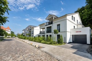 A residential street with modern houses, a cobblestone road, and a clear sky.