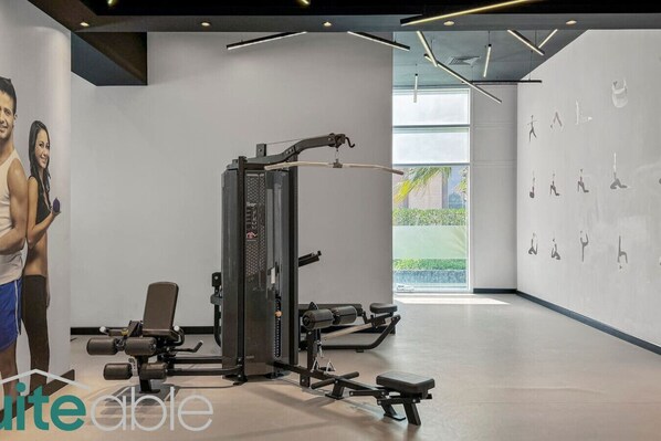 A modern gym with exercise equipment, a bench, and a wall with silhouettes of people exercising.