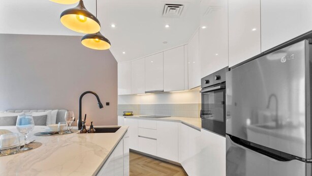 A modern kitchen with white cabinetry, a stainless steel refrigerator, and pendant lighting. - Spacious refurbished Studio steps away from metro (Dubai)