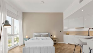 A modern hotel room with a large bed, a desk, and a kitchenette.