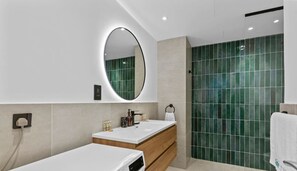 A modern bathroom with a large mirror, two sinks, a vanity, and a shower area with green tiles.