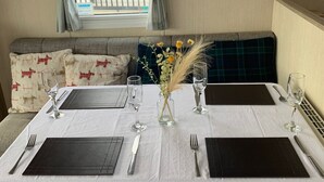A neatly set dining table with white tablecloth, black placemats, and wine glasses, in a room with a view of a balcony and a sign on the wall. - Seaside Retreat - Golspie Cabin (Golspie)
