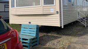 A mobile home with large windows, a ramp for accessibility, and a small outdoor area with a blue pallet. - Seaside Retreat - Golspie Cabin (Golspie)