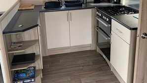 A compact kitchen with a gas stove, a microwave, and a sink. There is a window above the sink and a small shelf with a board game. - Seaside Retreat - Golspie Cabin (Golspie)