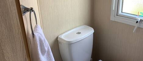 Een kleine, praktische badkamer met een wit toilet, een handdoek aan een metalen rek en een raam dat voor natuurlijk licht zorgt.