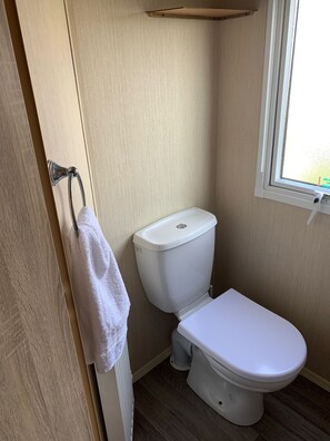 A small, compact bathroom with a white toilet, a towel hanging on a metal rack, and a window providing natural light.