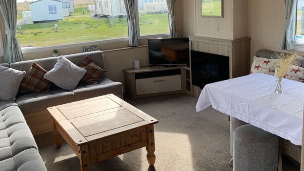 A cozy RV interior with a sofa, a coffee table, a TV, and a fireplace. - Seaside Retreat - Golspie Cabin (Golspie)