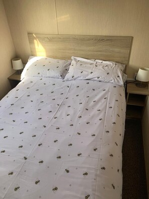 A hotel room with a neatly made bed, two bedside lamps, and a wooden headboard.