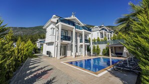 A modern two-story house with a swimming pool, a covered patio, and a mountain backdrop.