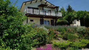 A two-story house with a balcony, surrounded by lush greenery and flowering plants. - House with swimming pool in exceptional surroundings (Ferrières-Poussarou)