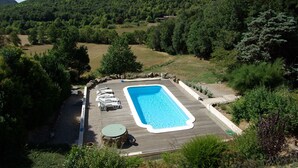 A rectangular swimming pool with a wooden deck, surrounded by greenery and a hilly landscape. - House with swimming pool in exceptional surroundings (Ferrières-Poussarou)