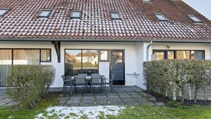 A house with a tiled roof, a front door, a small patio with a table and chairs, and a hedge in the front yard. - 3 bedroom accommodation in Nieuwpoort (Nieuwpoort)