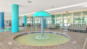 Zona de piscina con fuente central, mobiliario y entrada con cerramiento de vidrio.