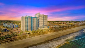 Un hotel de gran altura con varios pisos, una playa en primer plano y un cielo despejado.