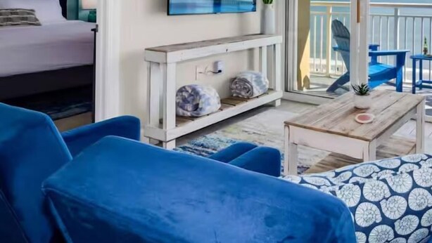 Una habitación con cama, televisión, balcón con vistas y muebles azules.