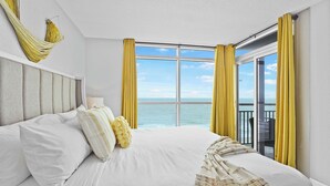 Una habitación de hotel con una cama grande, vistas al mar y cortinas amarillas.
