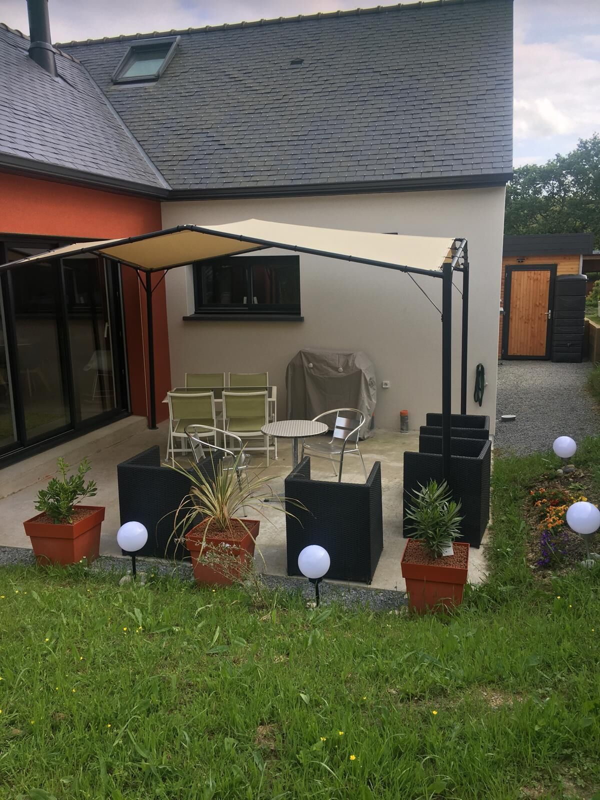 A modern house with a patio area featuring outdoor furniture, potted plants, and a covered seating area.