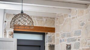 Un comedor con mesa de madera, sillas blancas, pared de piedra y puerta oscura.