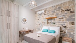 Un dormitorio con pared de piedra, una cama con colcha color beige, un escritorio de madera y un armario.