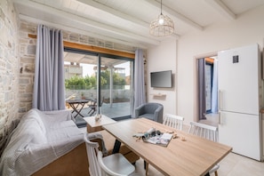 A cozy room with a wooden table, a sofa, a TV mounted on the wall, and a refrigerator. - Elmara Luxury Villa 3 - Next to the Beach (Faistos)