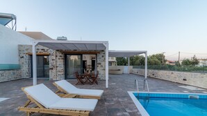 Un área de piscina en la azotea con dos sillas de descanso, una mesa y un espacio de estar cubierto.