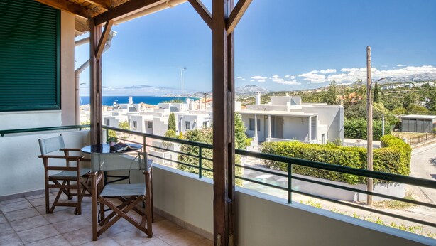 Varanda com vista para uma cidade costeira, móveis de madeira e uma janela com persiana verde.