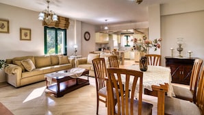 Uma sala de estar espaçosa com sofá, mesa de jantar e cadeiras, cozinha ao fundo e um lustre.