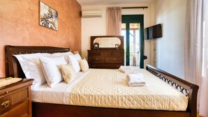 Uma cama bem arrumada com cobertura acolchoada, uma cômoda de madeira com gavetas, uma TV de tela plana na parede e um quadro emoldurado na parede.