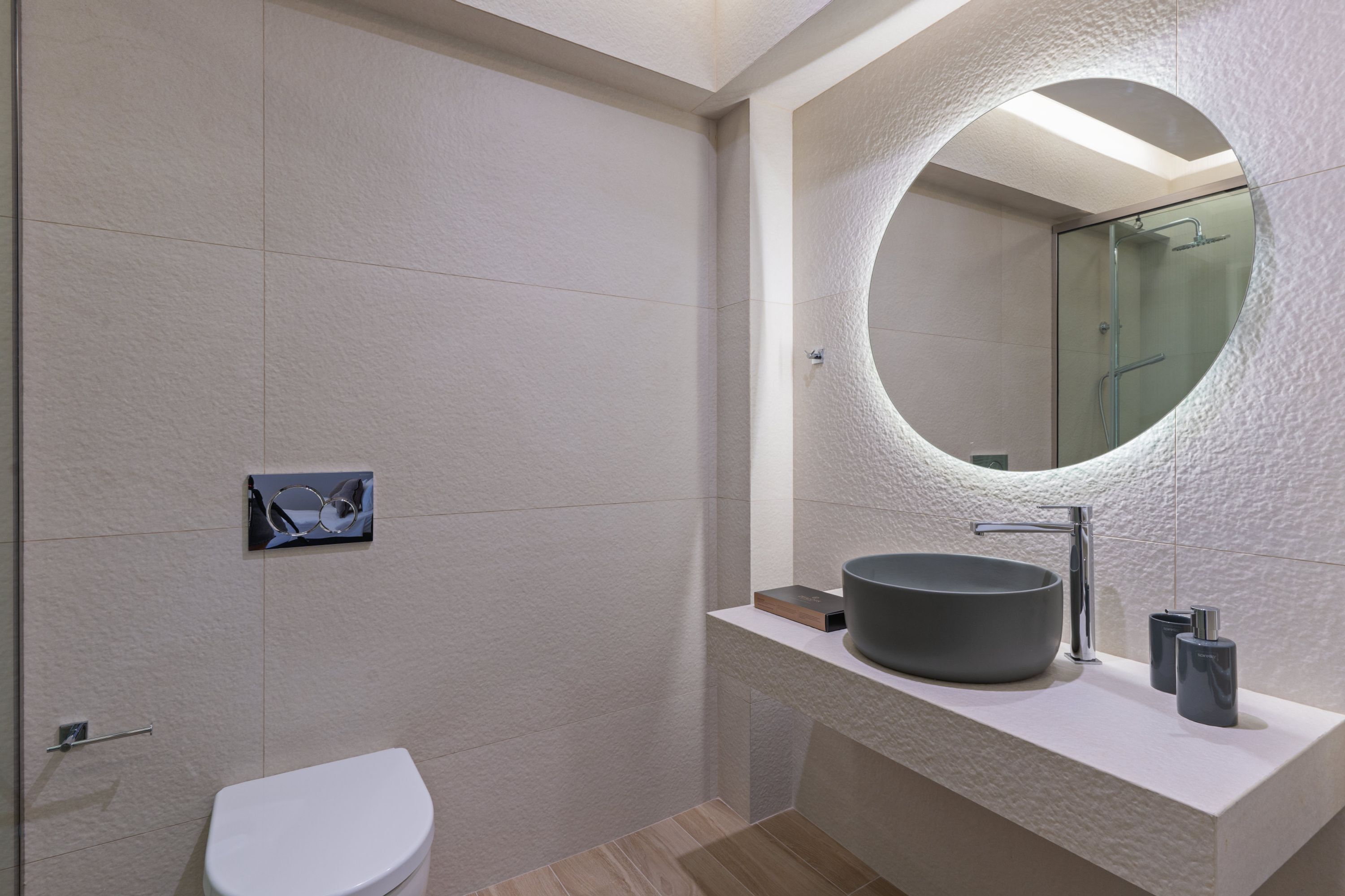 A modern bathroom with a round mirror, a vessel sink, and a toilet.
