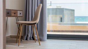 En moderne stol med træben og polstret sæde, placeret ved siden af et vægmonteret skab med mønstrede døre, i et rum med et stort vindue med udsigt over en by.