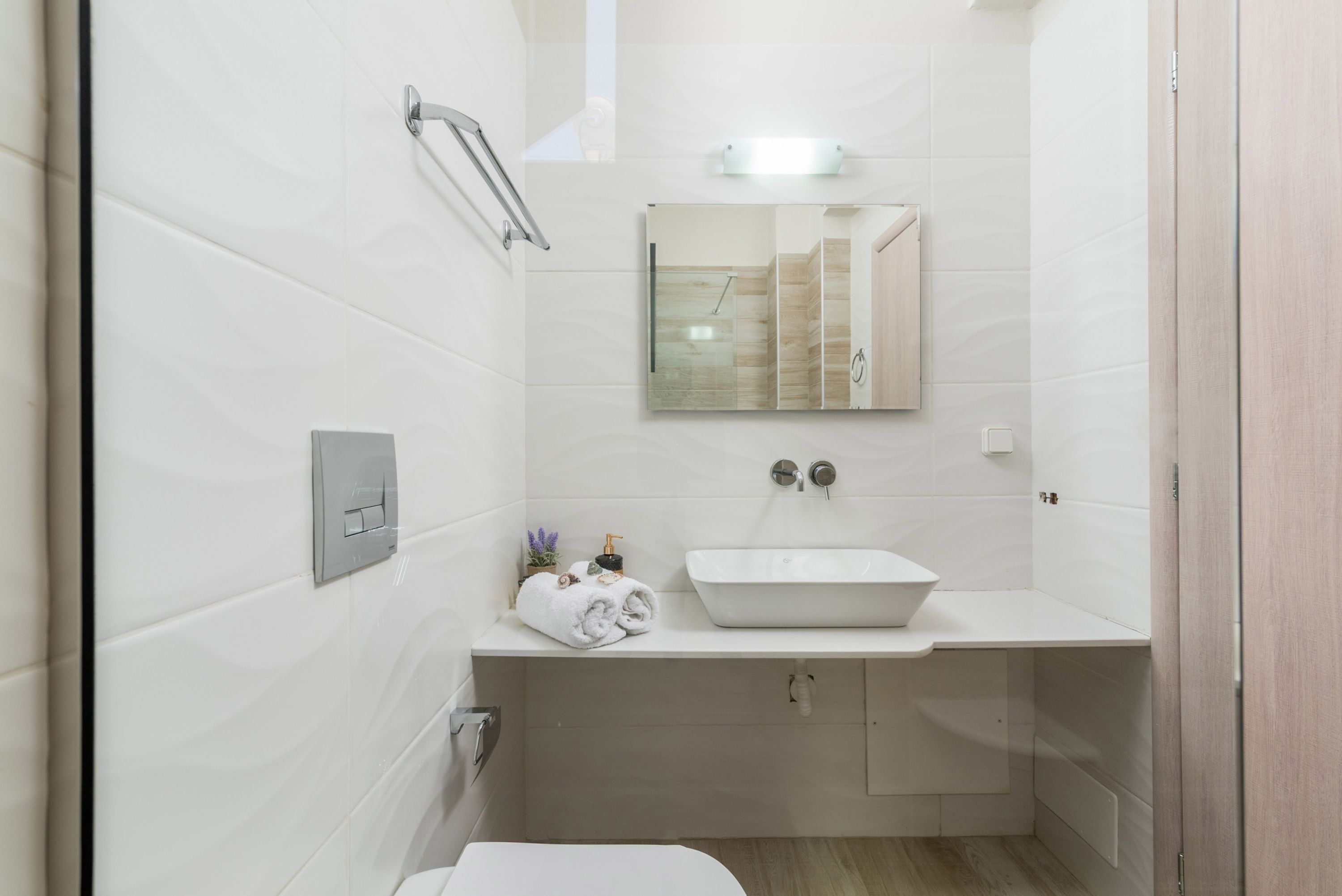 A bathroom with white tiles, a white sink, a mirror, and a towel rack.