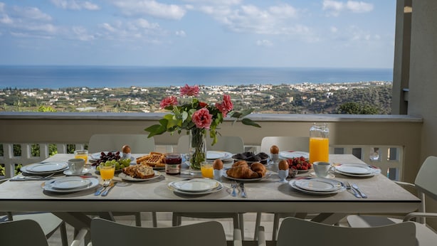A breakfast table with plates, cutlery, and a vase of flowers, overlooking a coastal view. - Villa Panorama - With 60m Private Pool (Rethymno)