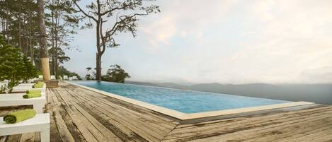A wooden deck with a pool, surrounded by trees and overlooking a mountainous landscape.