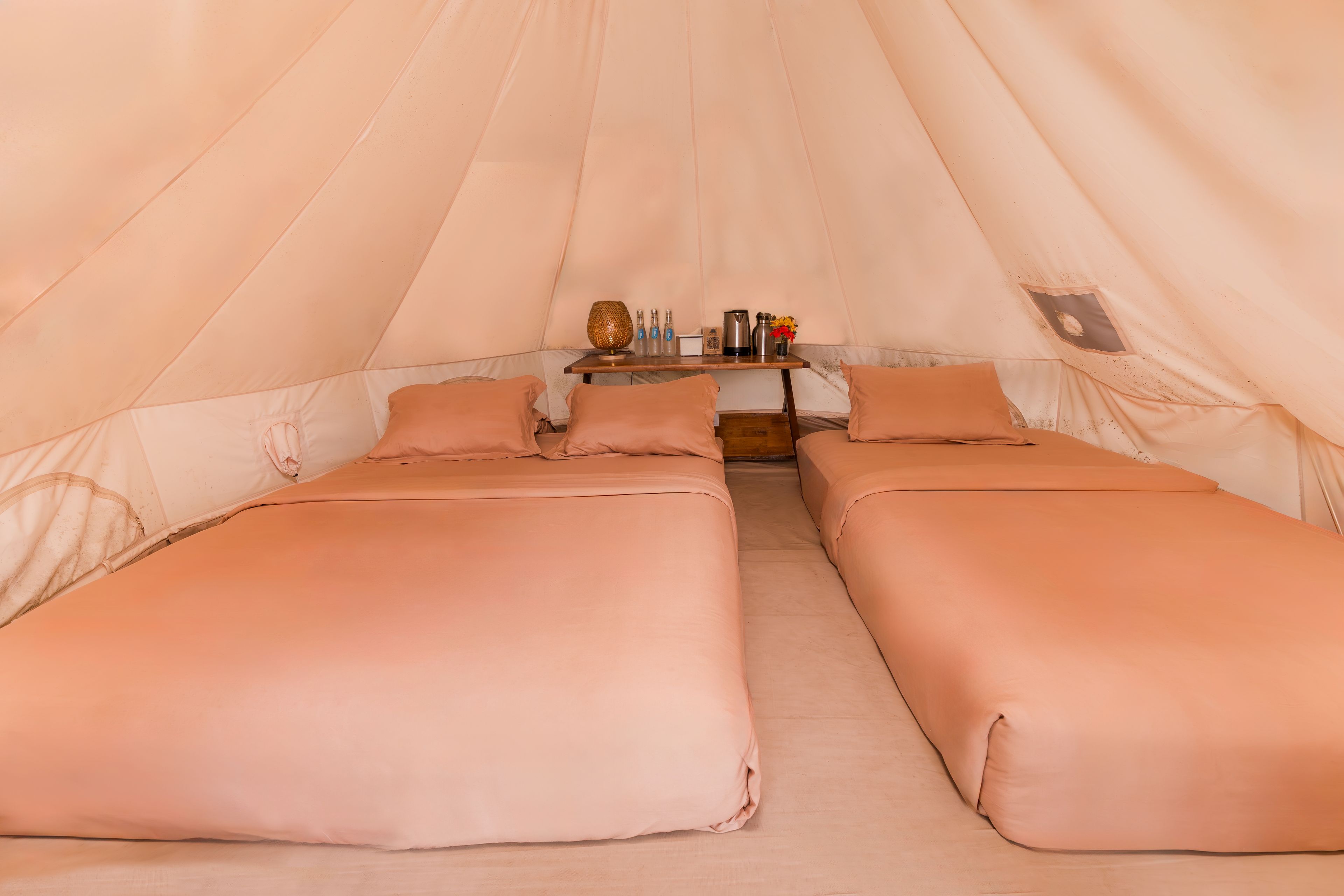 Een tent met twee bedden, een tafel met een lamp en een raam.