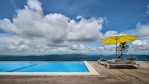 Una terraza de madera con piscina, sillones de descanso y una sombrilla amarilla.