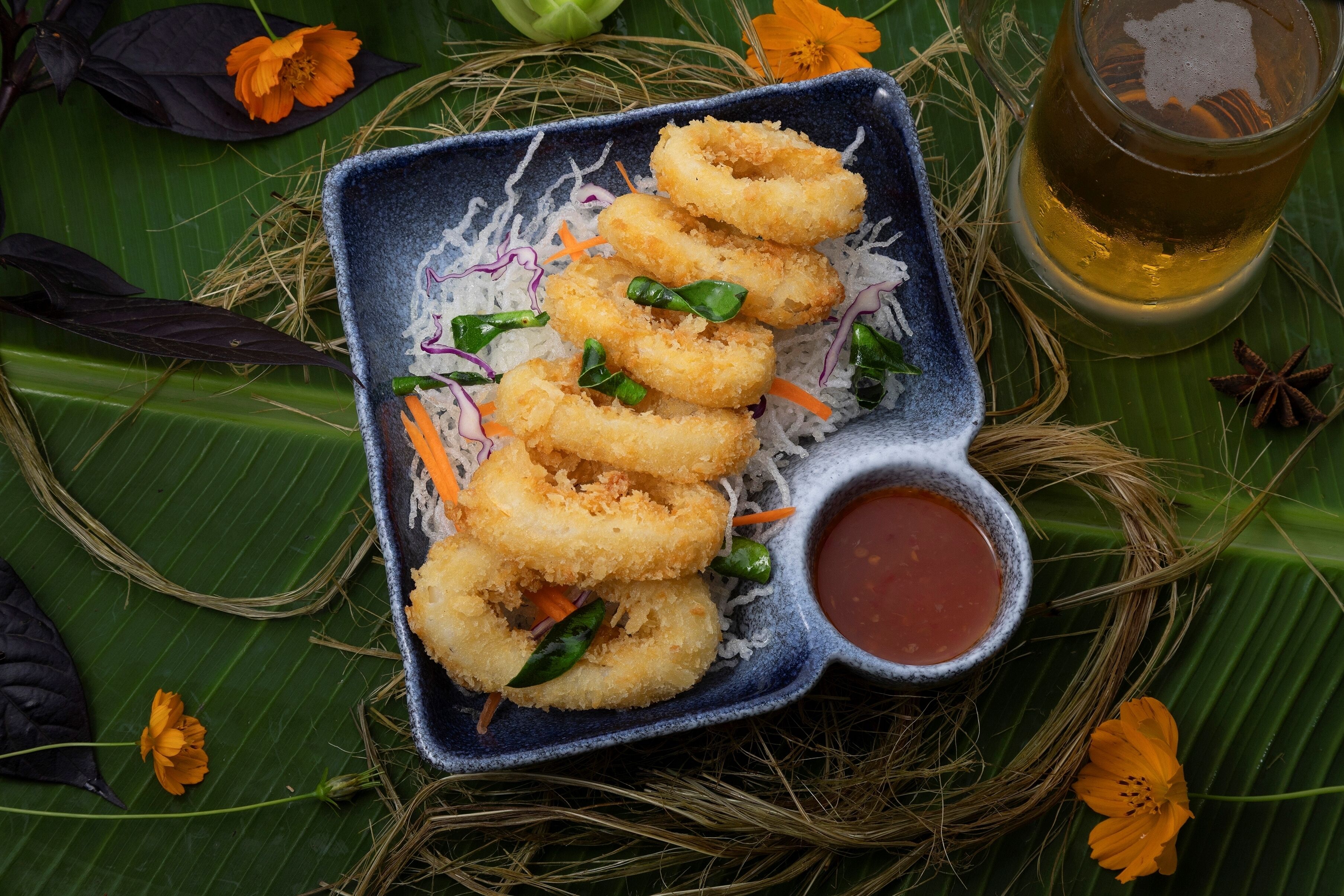 A plate of fried snacks with a side of dipping sauce, set on a green leaf background.