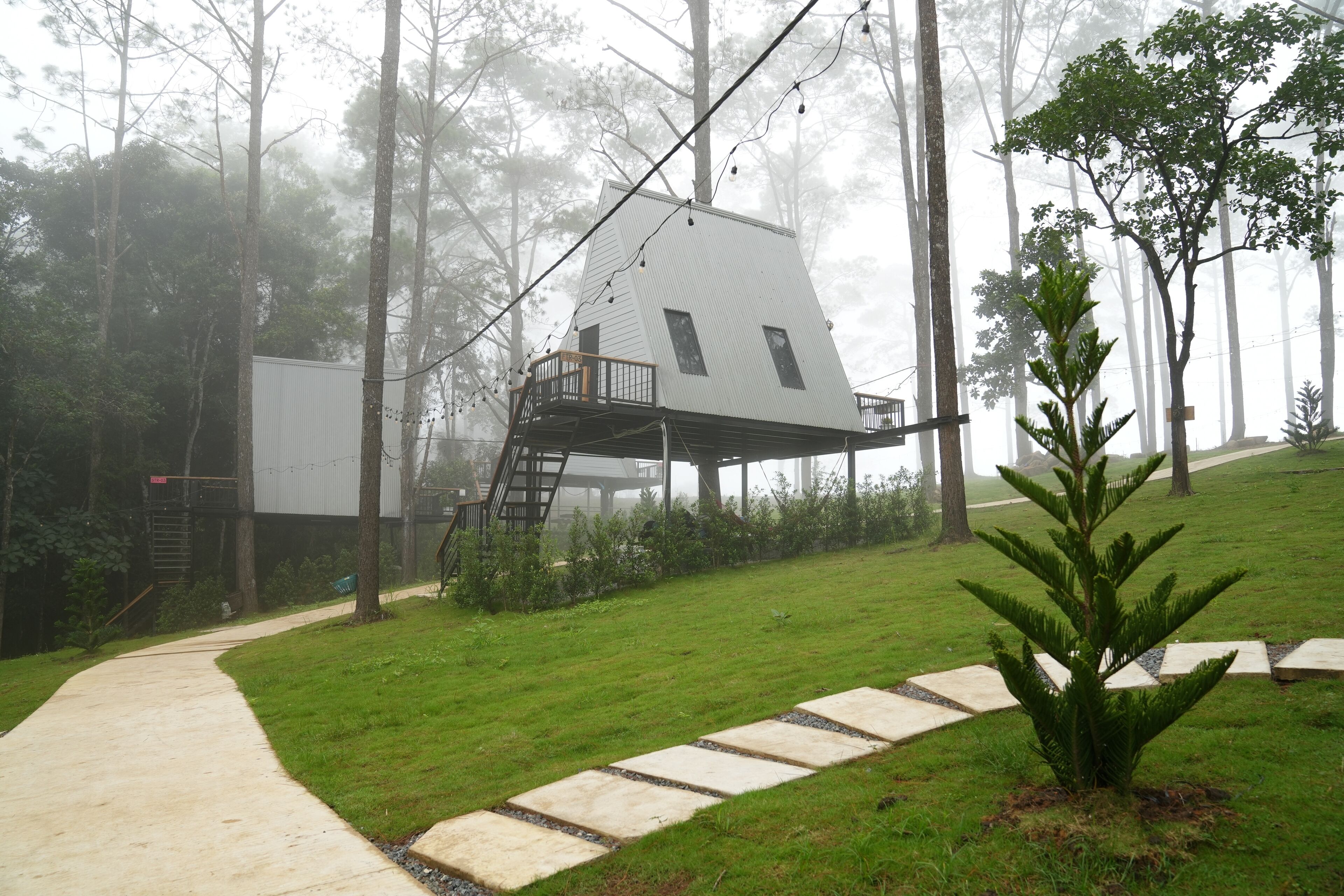 Uma casa na árvore com varanda, rodeada por um gramado e árvores.