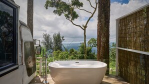 Un jacuzzi grande y blanco en una terraza de madera, con vistas a árboles y montañas.