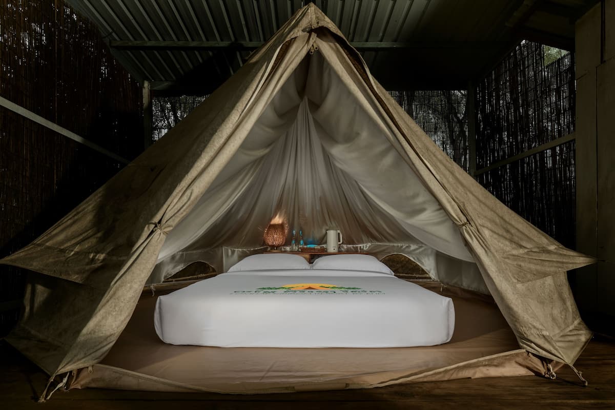 Alojamiento en tienda de campaña con cama, una mesa con lámpara y una ventana.