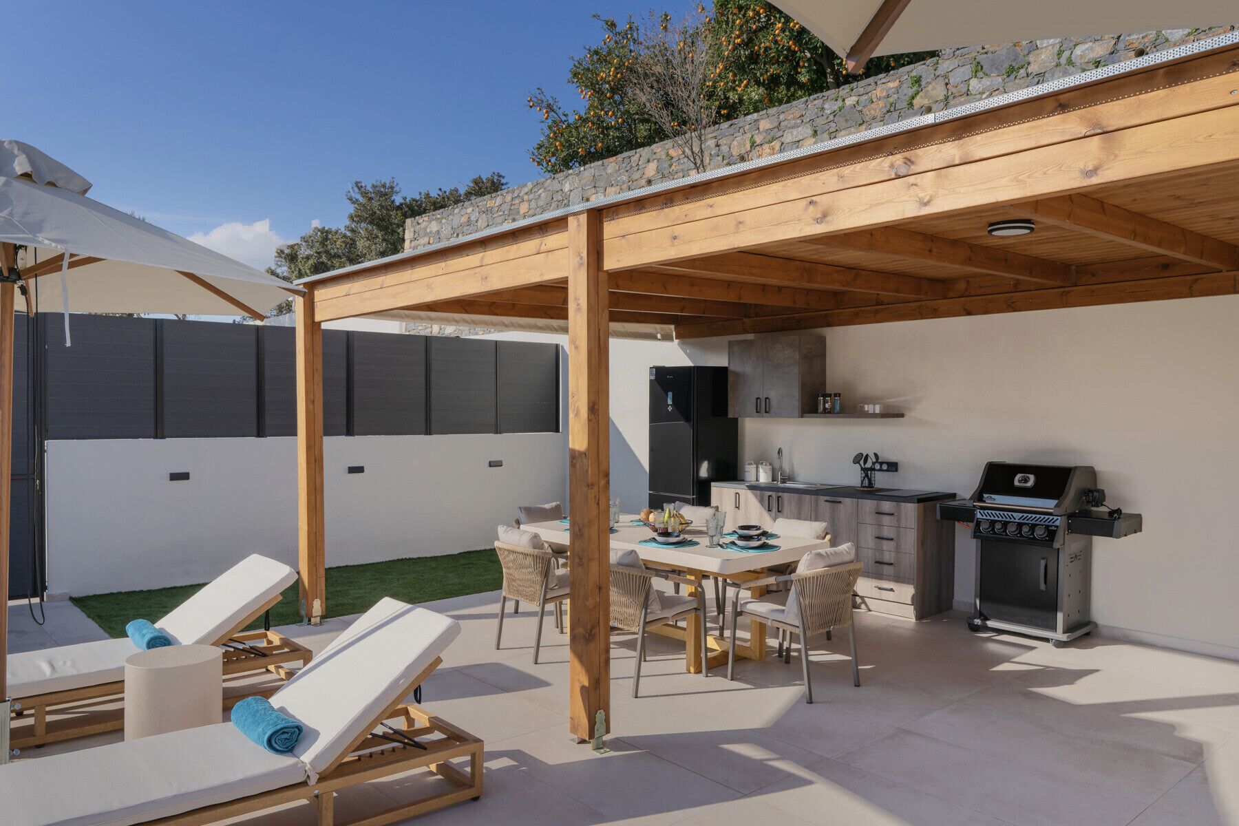 Un patio techado al aire libre con mesa, sillas, una parrilla y sillones de descanso.