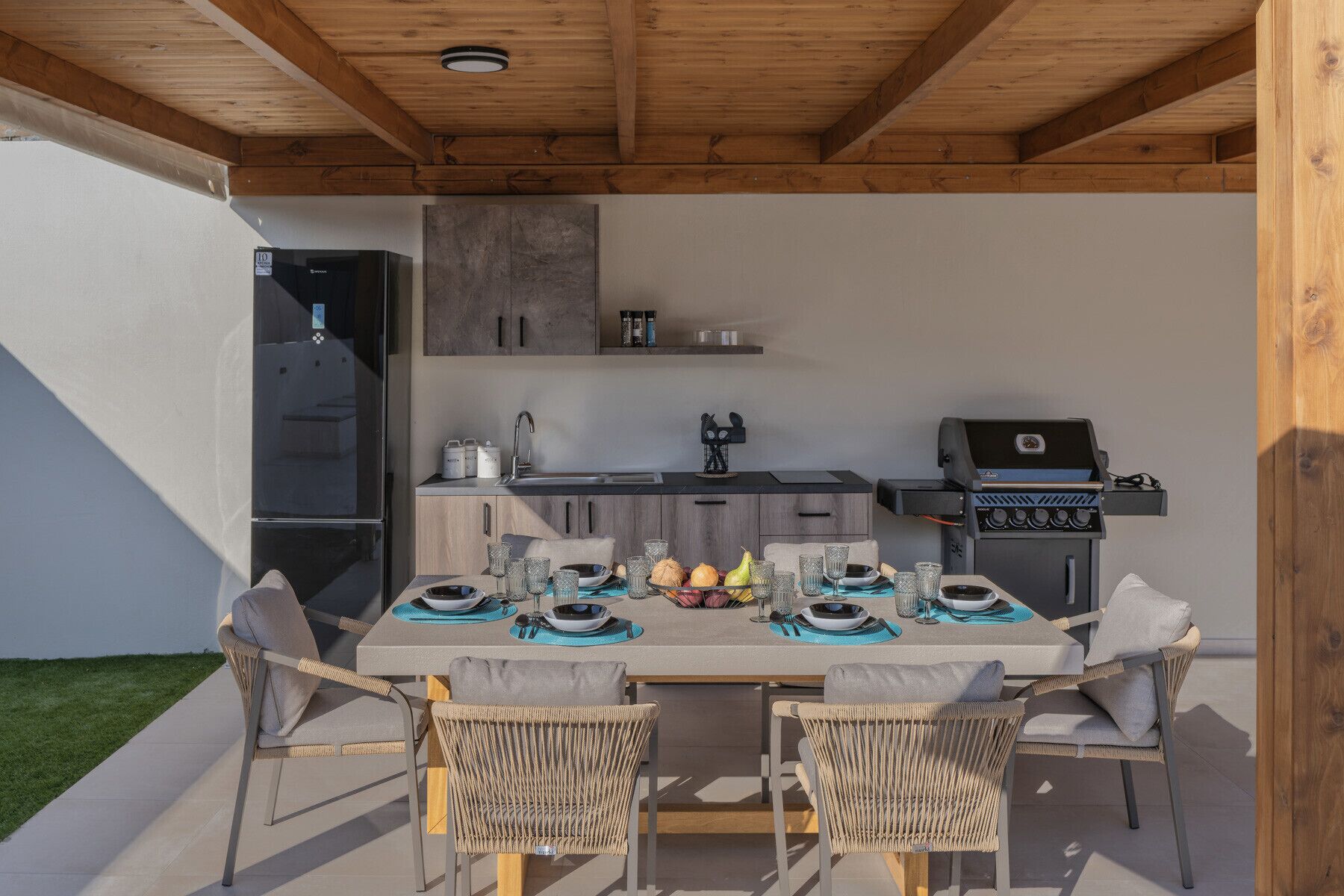 Une cuisine extérieure avec une table à manger pour quatre personnes, entourée de chaises en osier.