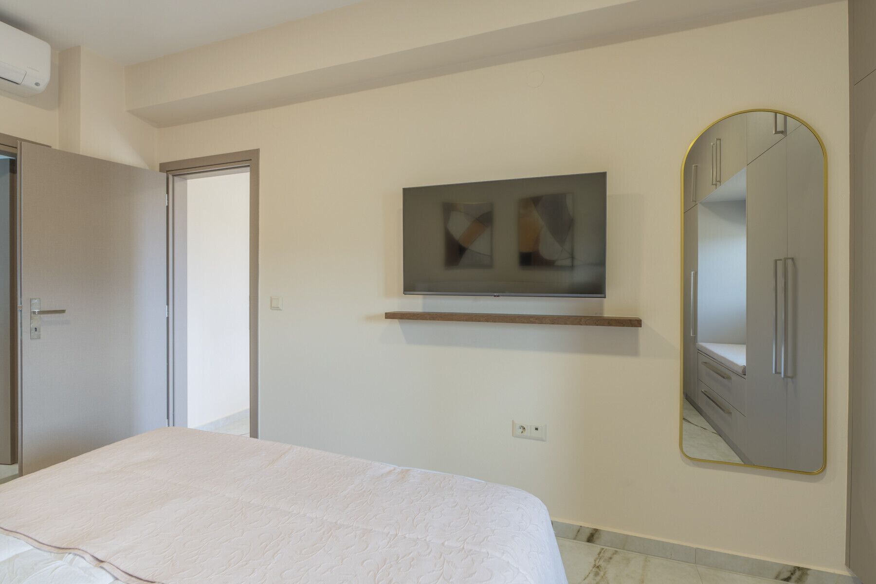A bedroom with a bed, a television mounted on the wall, a mirror, and a wardrobe.