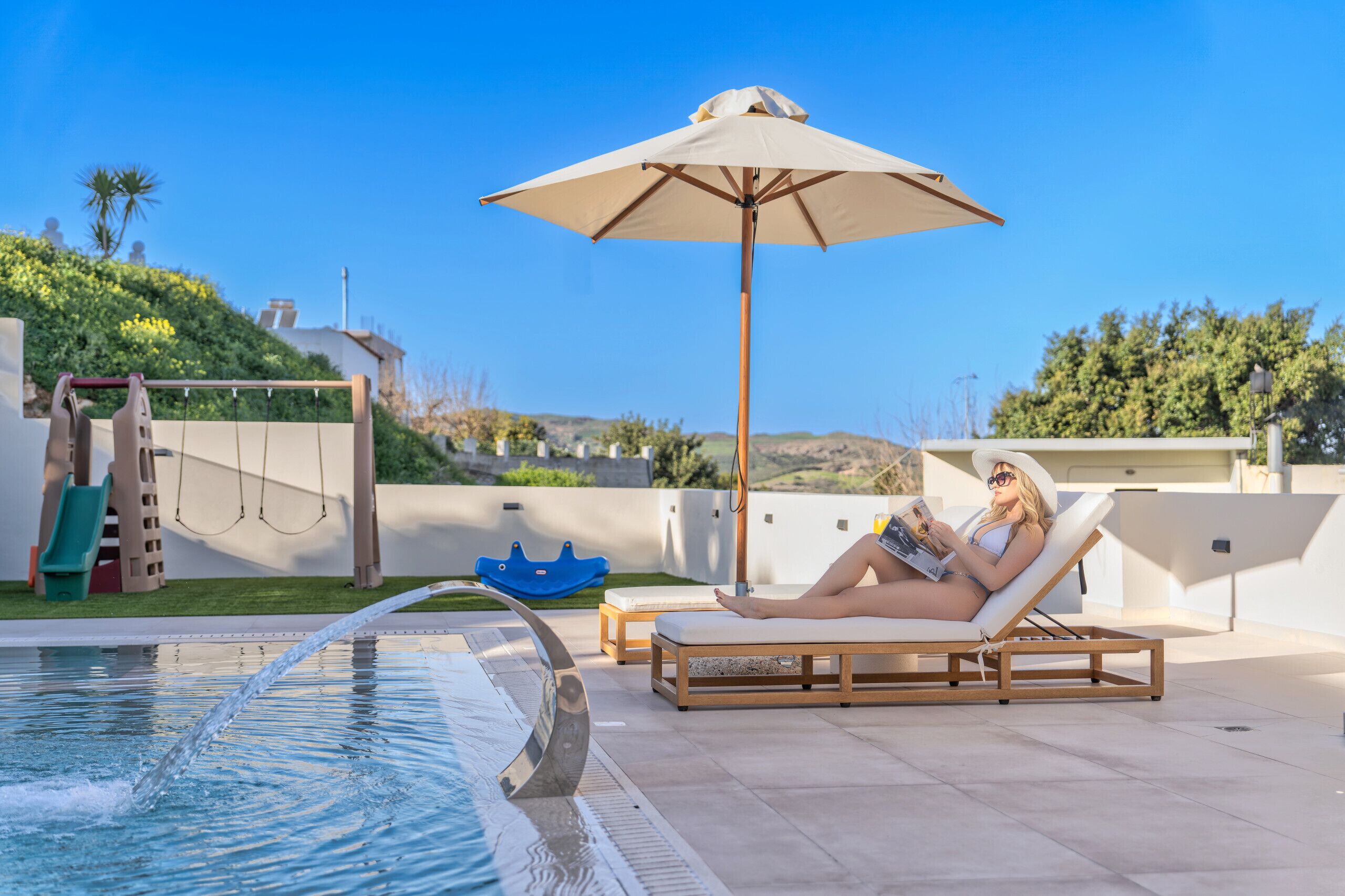 A poolside area with a lounge chair, a water feature, and a large umbrella.
