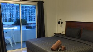 A modern hotel room with a large bed, a nightstand, a lamp, and a view of a building through a sliding glass door. - Smart Place Pattaya (Pattaya)
