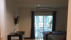 A hotel room with a desk, a chair, two beds, and a large window with a view of buildings. - Smart Place Pattaya (Pattaya)