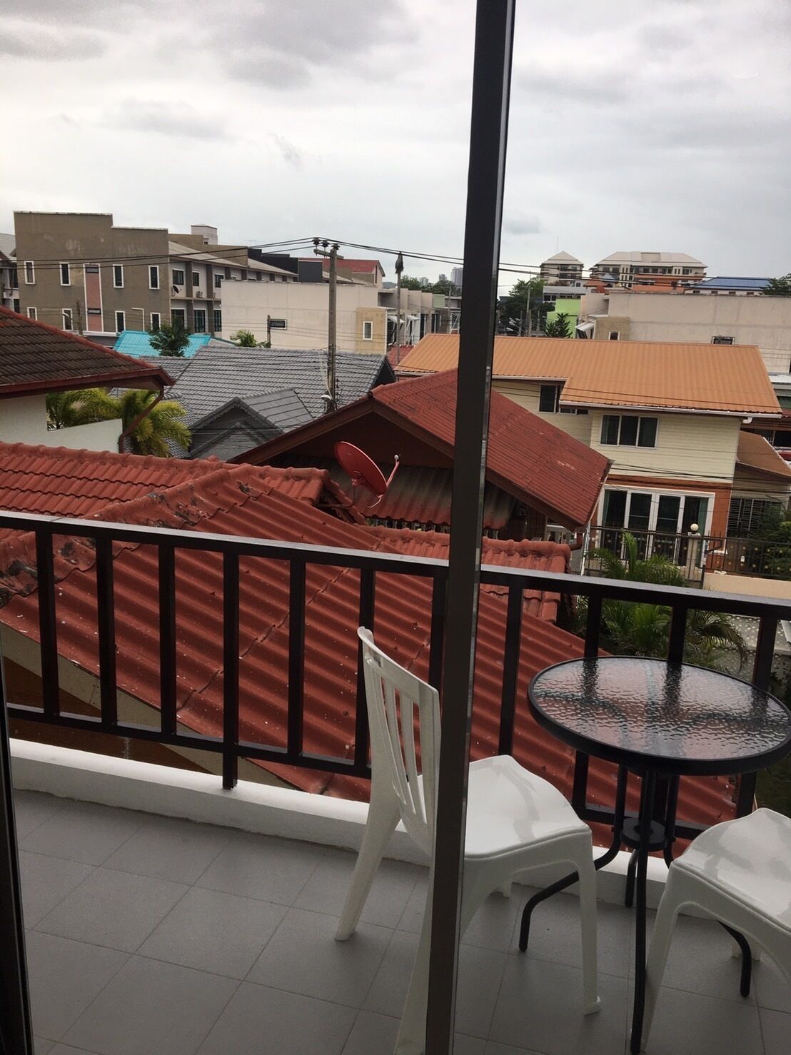 Varanda com telhado vermelho, cadeiras brancas e uma mesa redonda pequena.