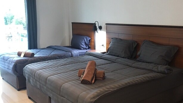 A modern hotel room with two beds, a large window with curtains, a bedside table with a lamp, and a view of the outside. - Smart Place Pattaya (Pattaya)