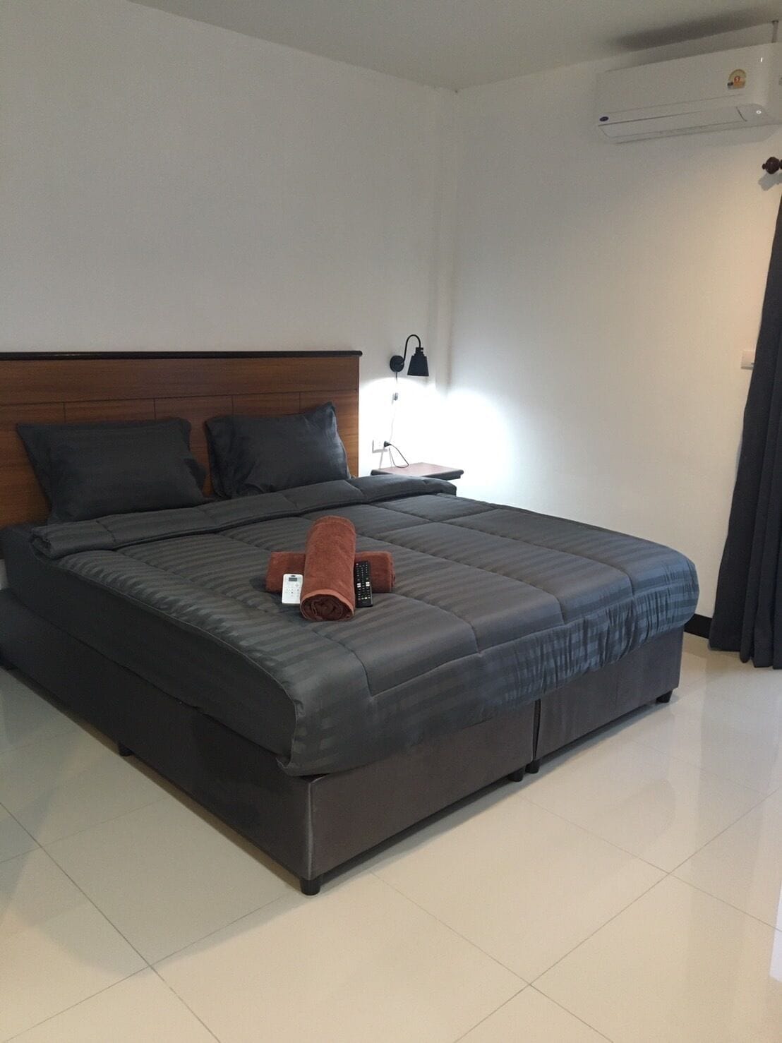 A modern hotel room with a large bed, a nightstand, a lamp, and an air conditioning unit.